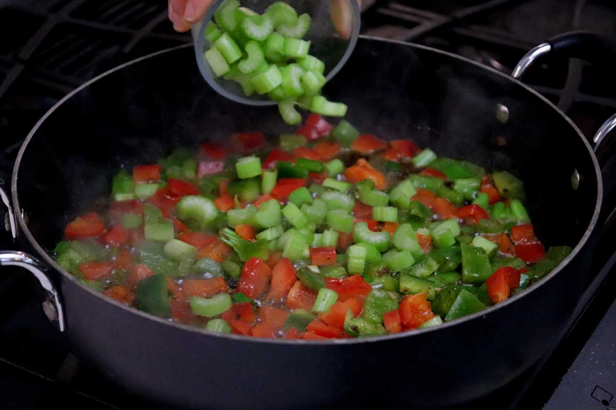 Pouring celery into vegetable mix in cast iron skillet