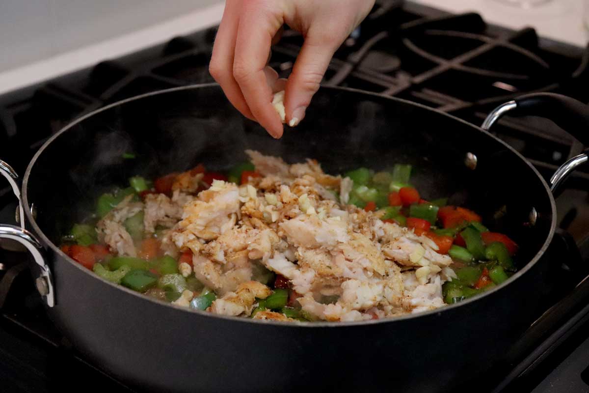 Adding garlic to catfish and veggies in cast iron skillet