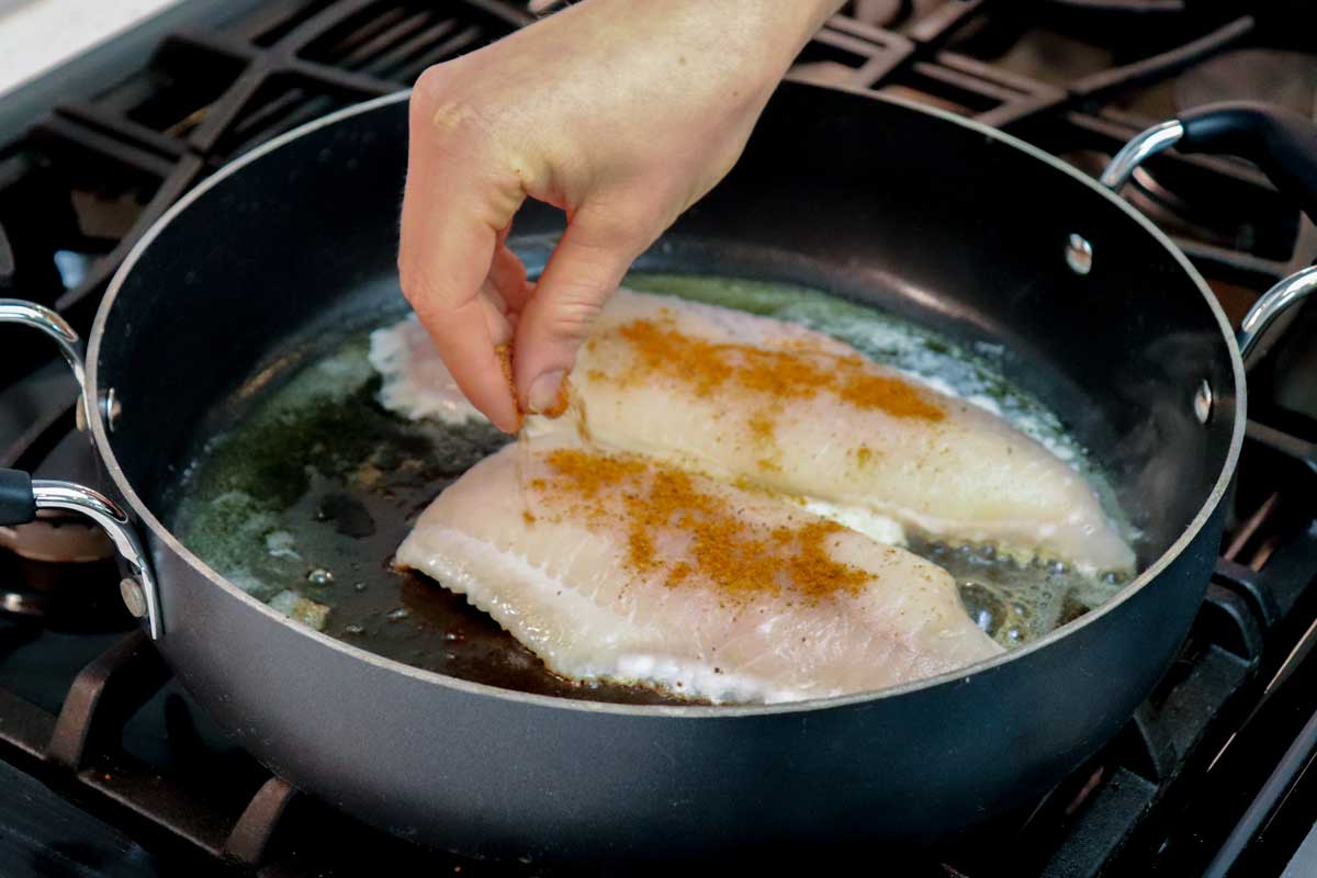 Catfish fillets being seasoned in cast iron skillet