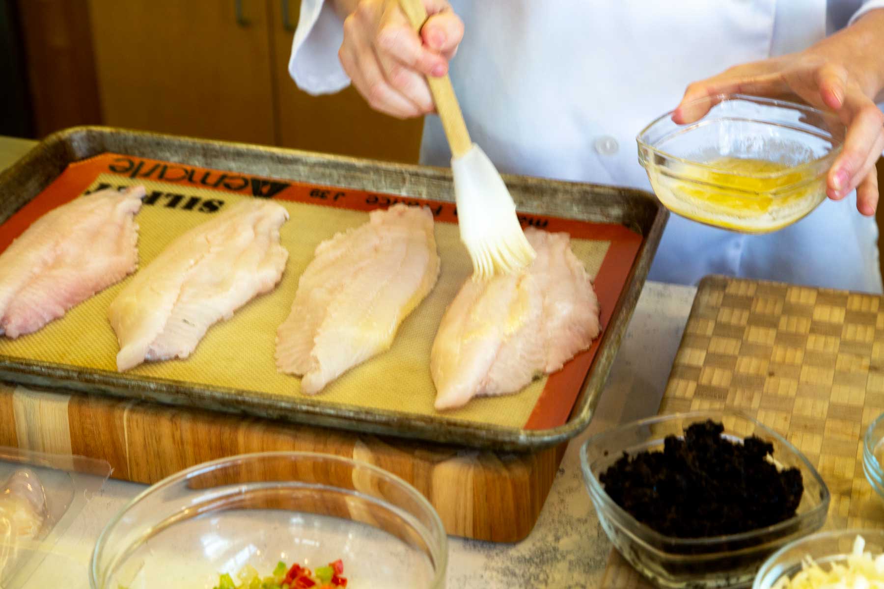 Brushing butter onto catfish fillets on baking sheet