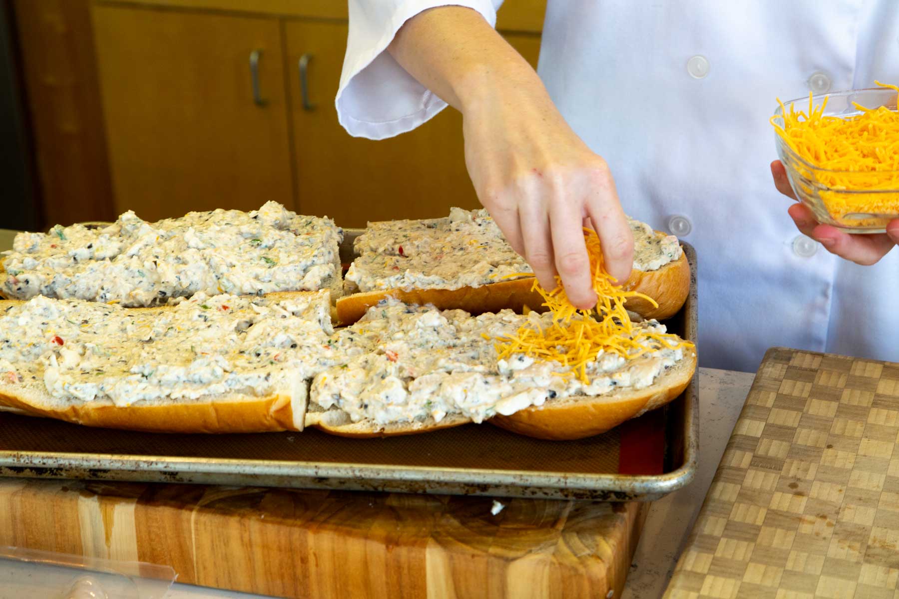 Catfish spread on french bread, sprinkling cheddar cheese on top