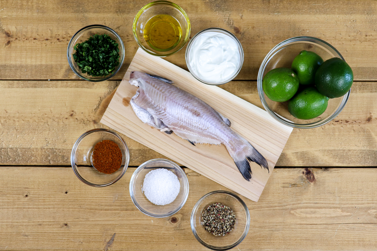 Grilled catfish ingredients including whole fish, spices and limes