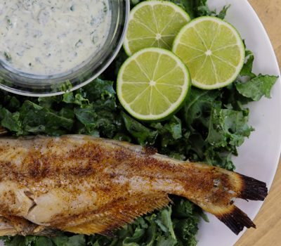 whole grilled catfish with seasoning and sauce on a bed of greens
