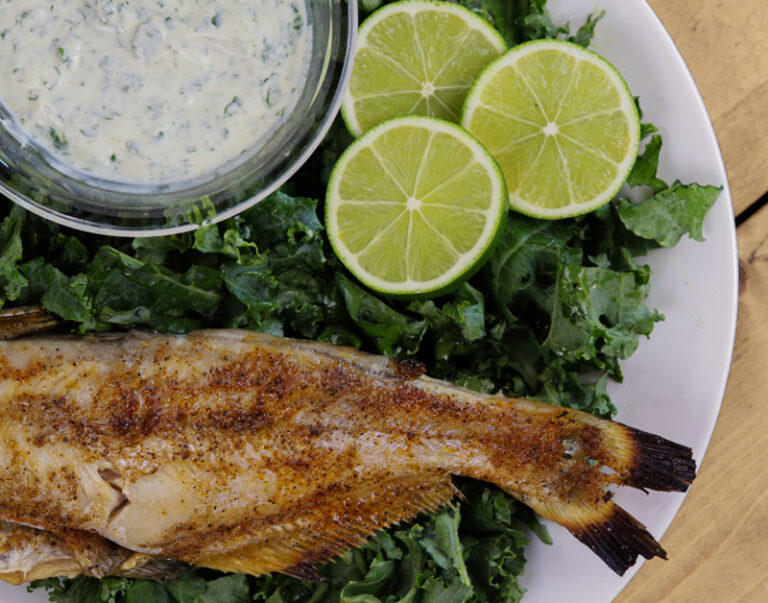 whole grilled catfish with seasoning and sauce on a bed of greens