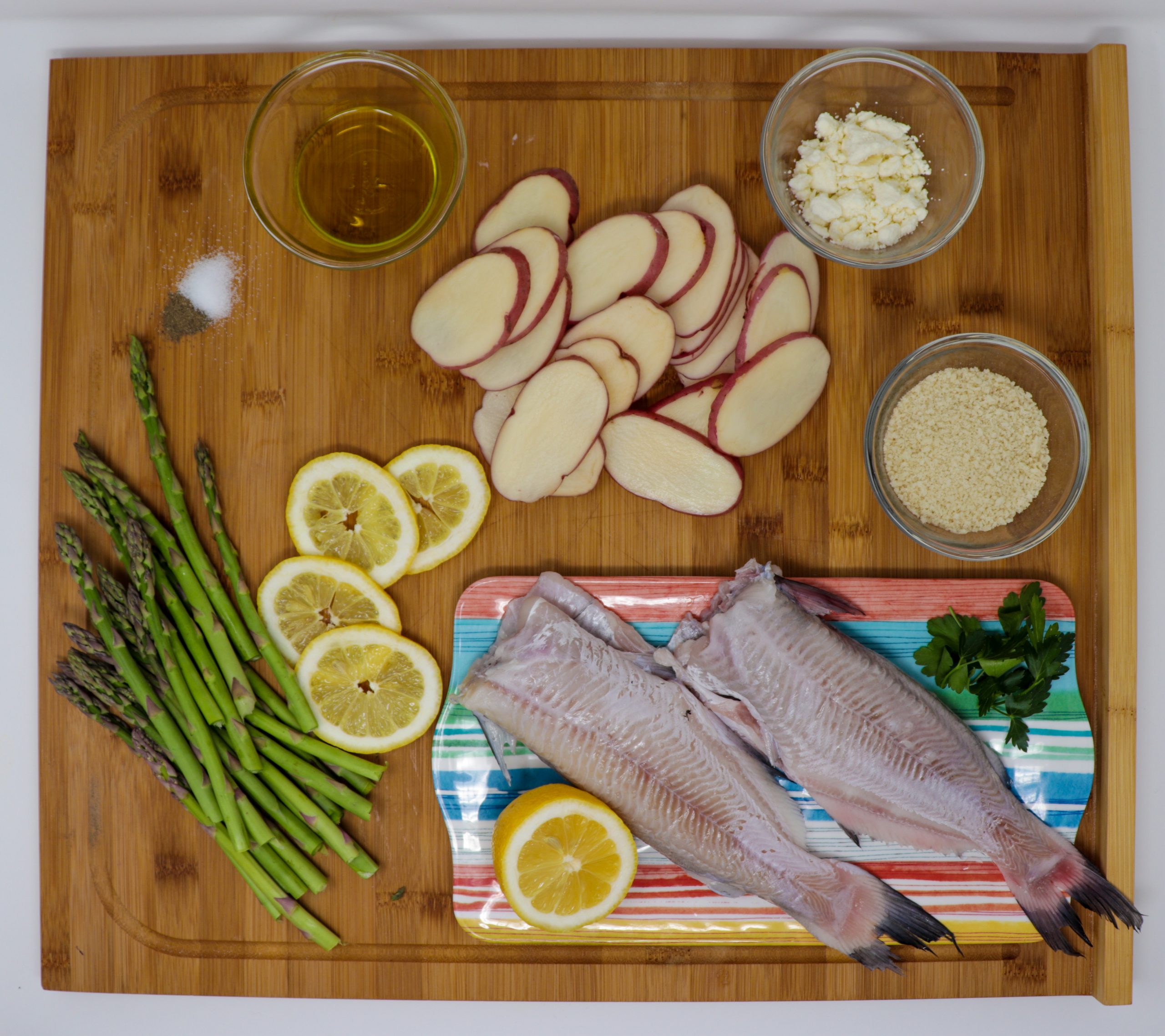 Baked catfish ingredients including whole fish, red potatoes, lemons, asparagus and garlic