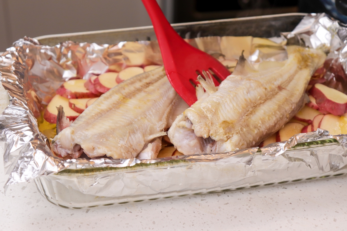 Adding catfish to baking pan with potatoes