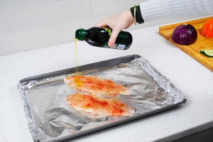 pouring olive oil on seasoned catfish fillets