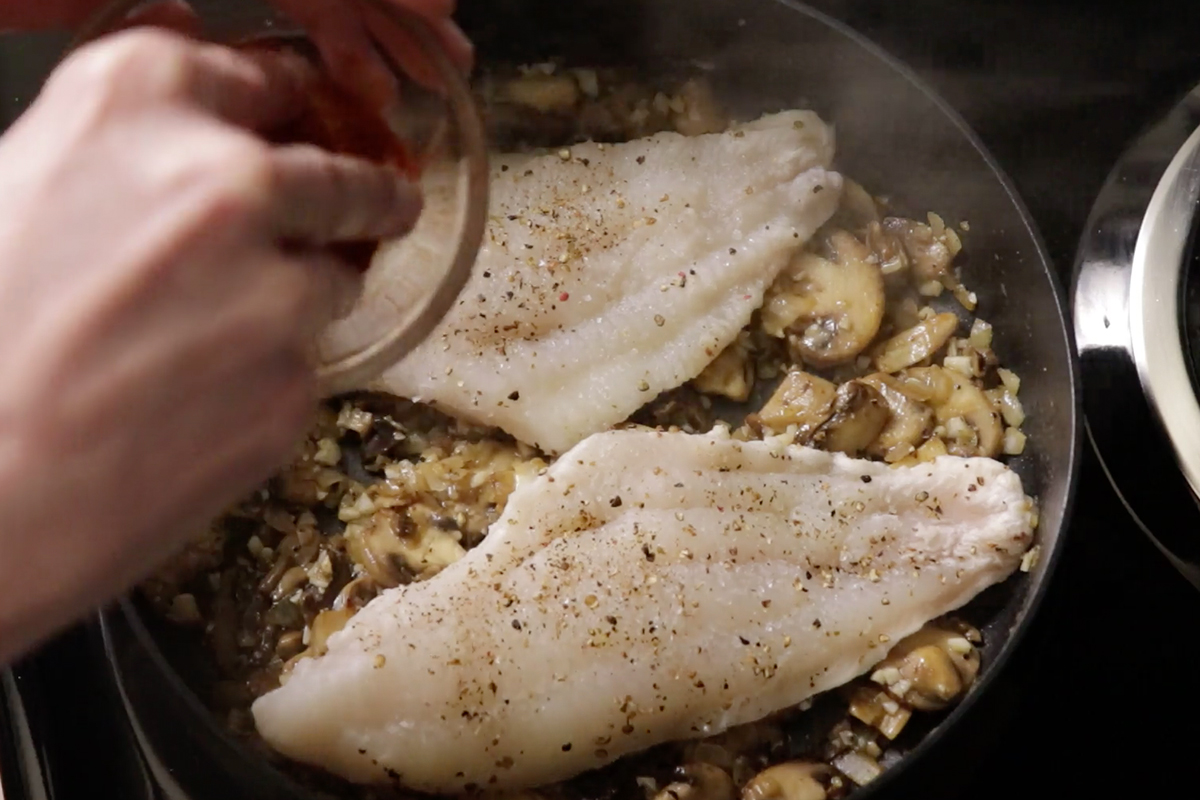 seasoned catfish fillets cooking on top of mushrooms on stove