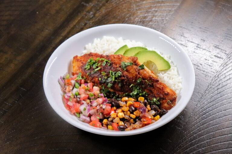 Blackened catfish fillet served in a bowl with white rice, avocado slices, pico de gallo, and a corn and black bean salsa.