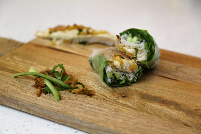 Heartland Catfish spring rolls sliced in half on a wooden board, filled with lettuce, cucumber, and fried catfish, garnished with crispy shallots and cilantro.