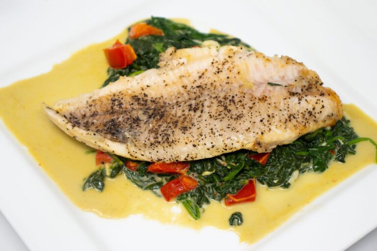Seared catfish fillet served over sautéed spinach with diced tomatoes in a butter sauce.