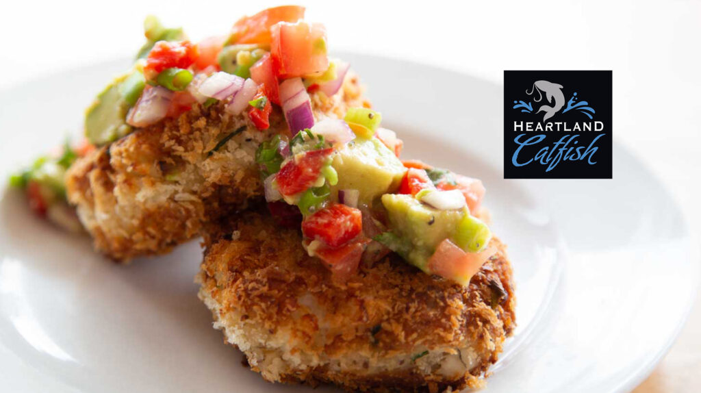 Breaded catfish cakes topped with avocado and tomato salsa, plated with the Heartland Catfish logo.