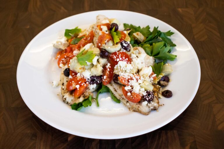 Grilled catfish fillet topped with diced tomatoes, artichoke hearts, olives, and feta cheese, served with fresh parsley.