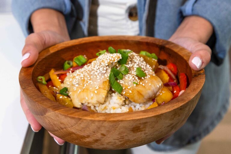 Close-up of a bowl of catfish on a bed of rice and vegetables.