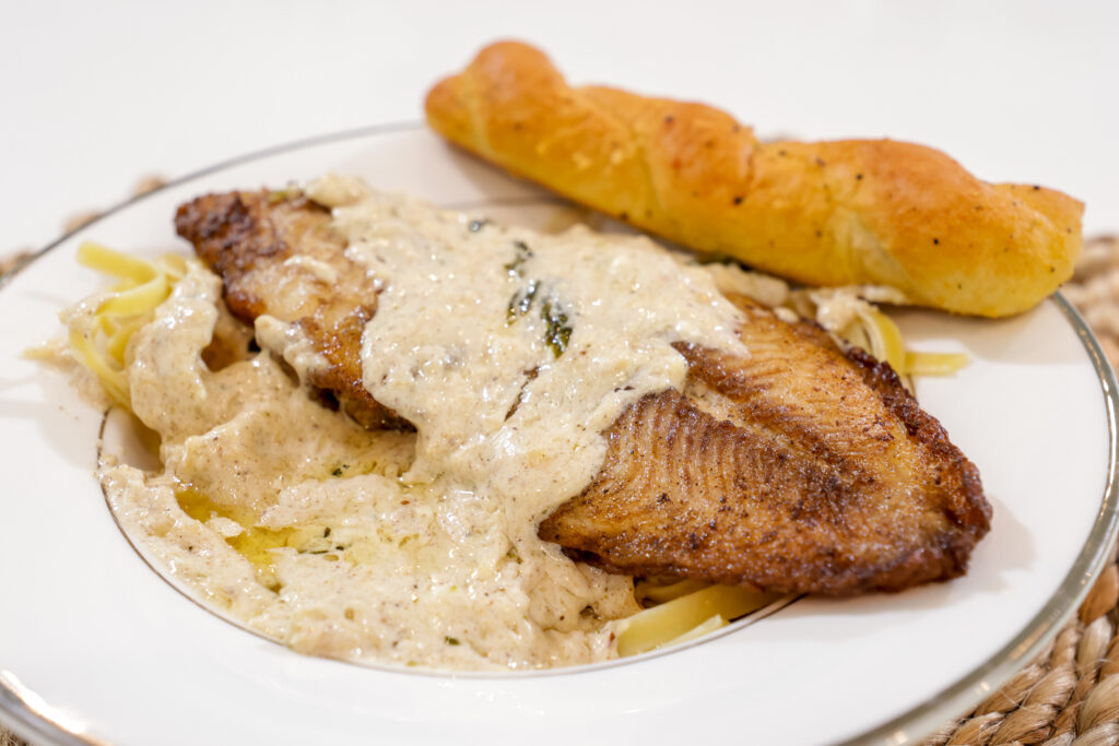 Catfish fillet served over fettuccine Alfredo pasta