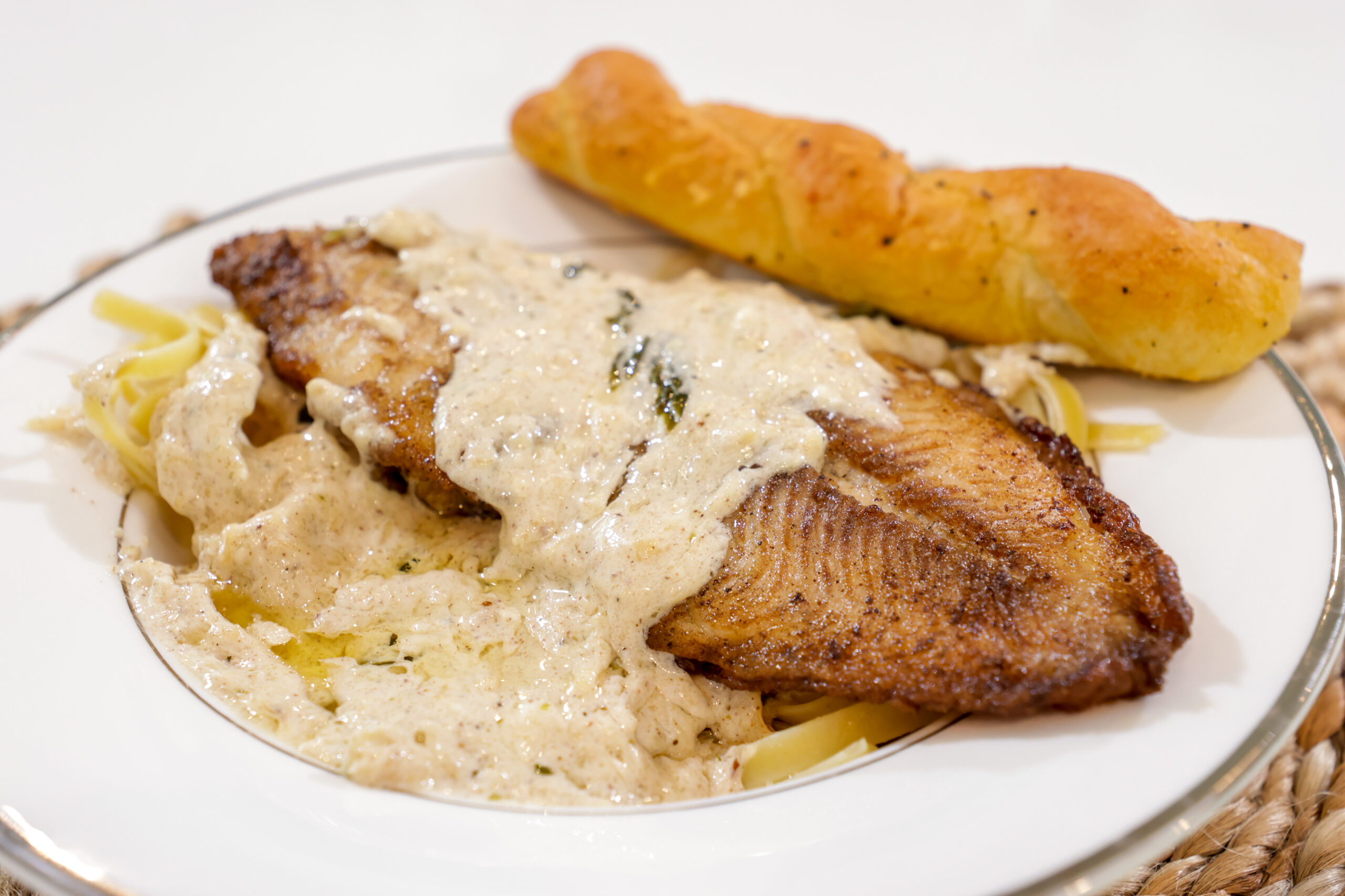 Catfish fillet served over fettuccine Alfredo pasta
