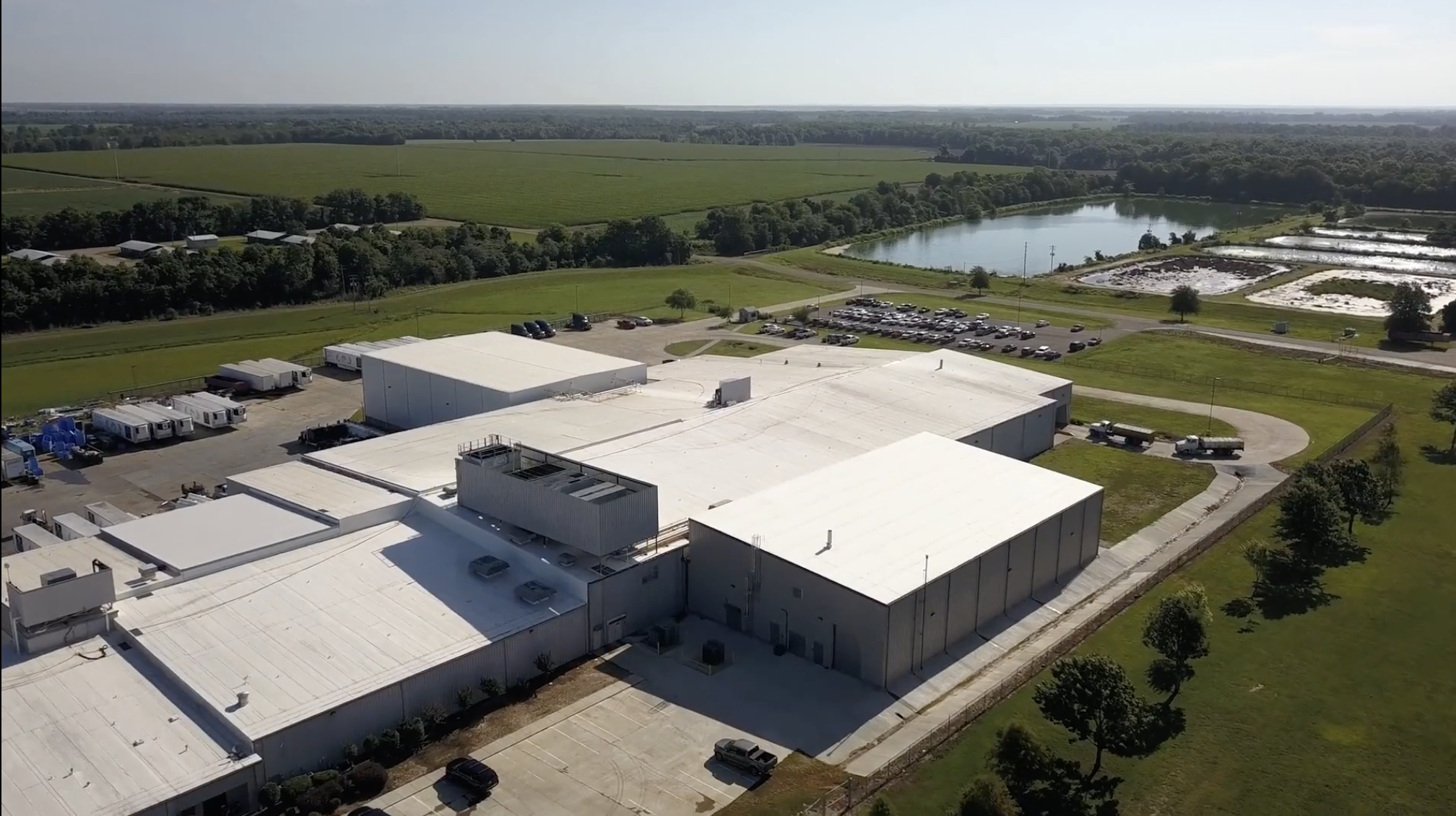 Aerial view of the Heartland Catfish processing plant surrounded by catfish ponds, farmland, and a parking lot with employee vehicles and delivery trucks.