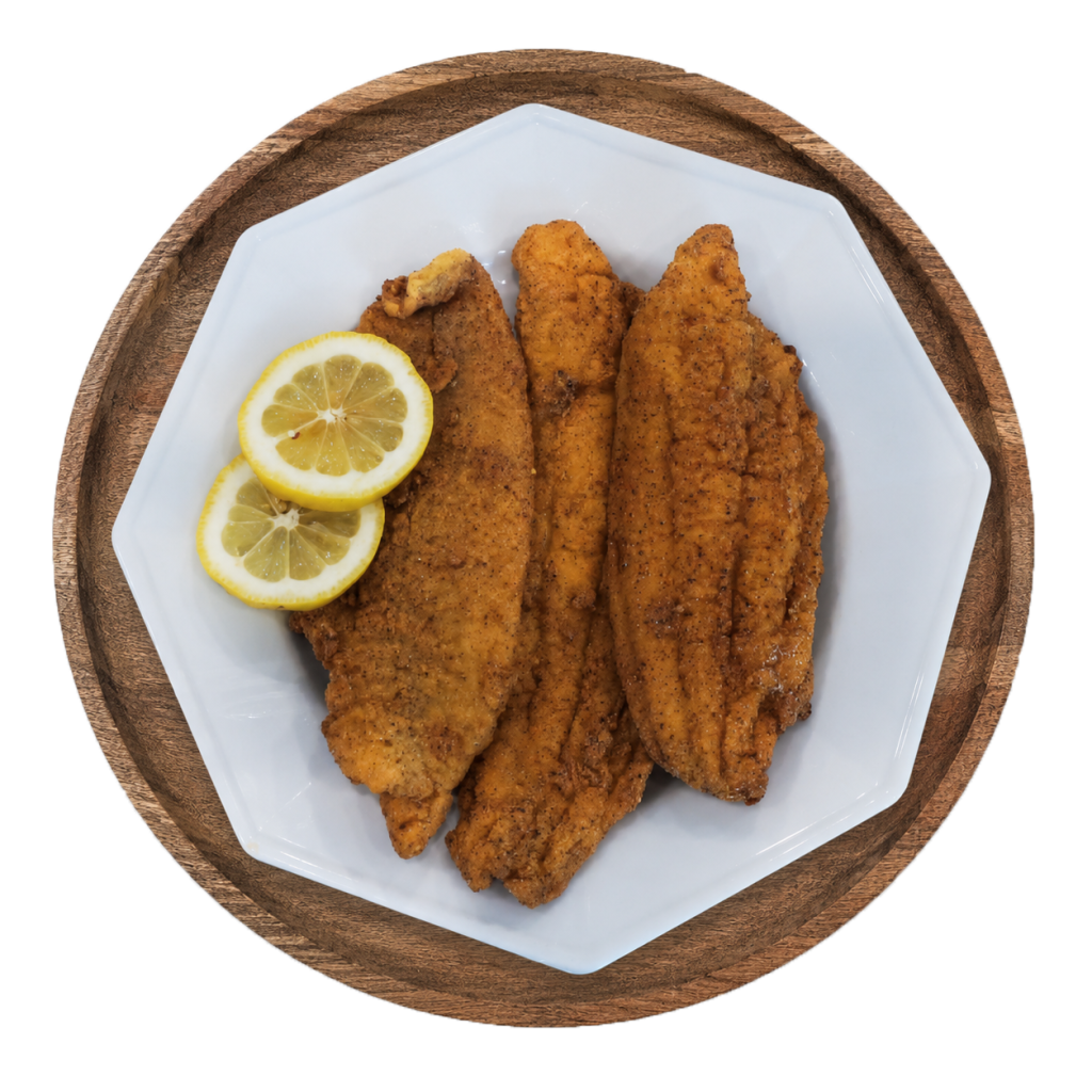 Three fried catfish fillets with lemon slices on a white plate over a wooden charger.