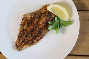 Grilled catfish on a white plate with a lemon.