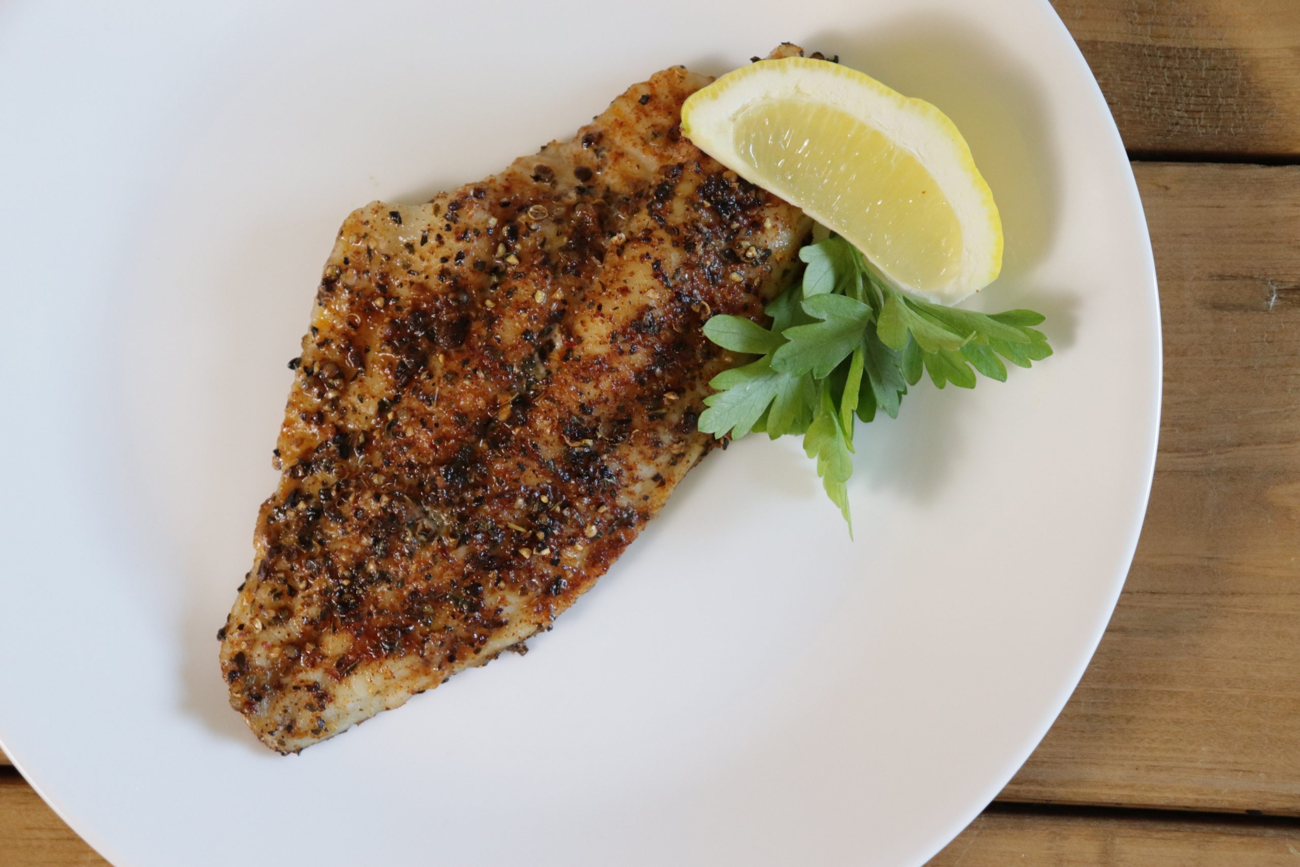 Grilled catfish on a white plate with a lemon.