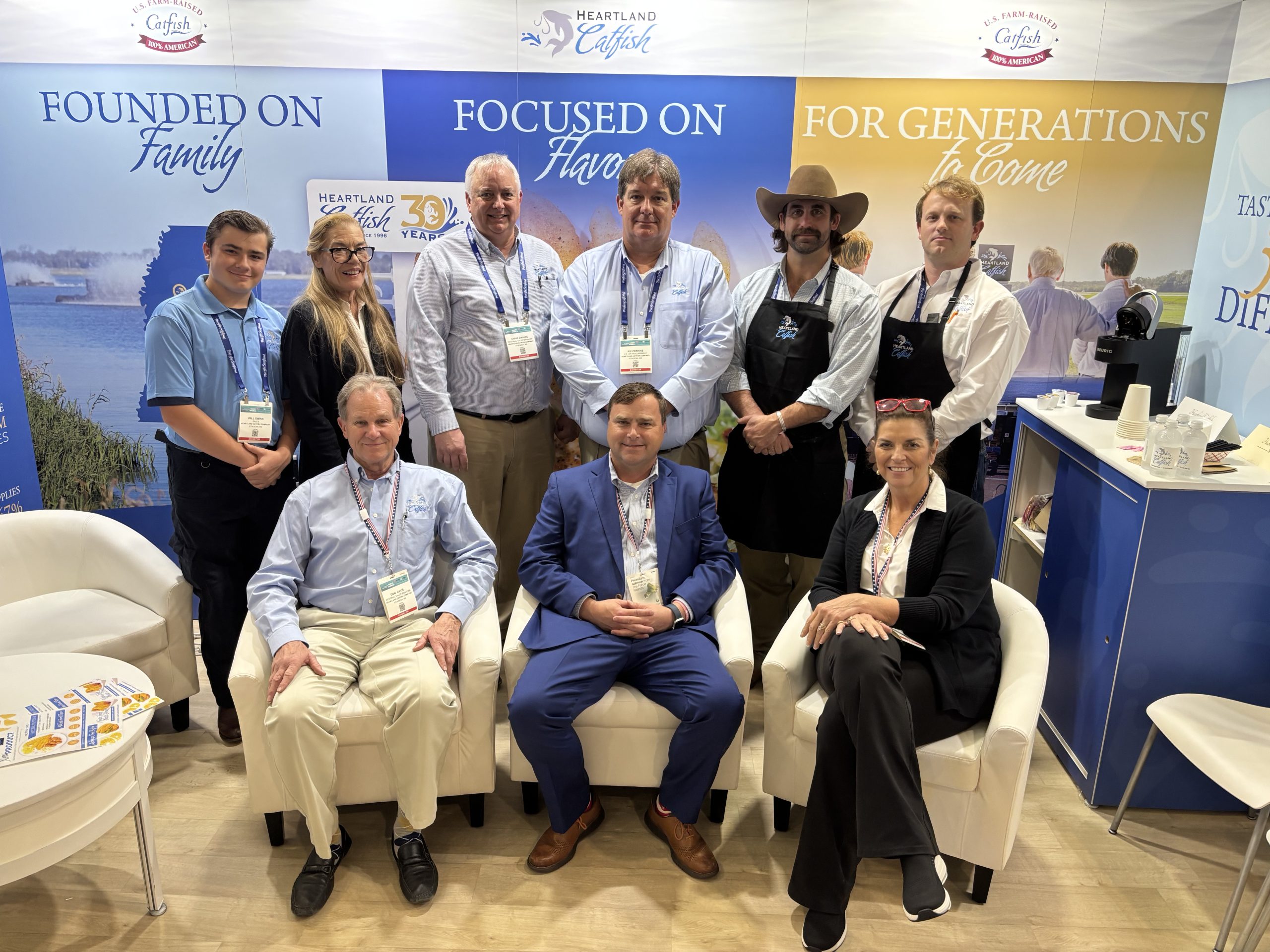 Heartland Catfish team posing at a trade show booth with banners reading Founded on Family, Focused on Flavor, For Generations to Come.