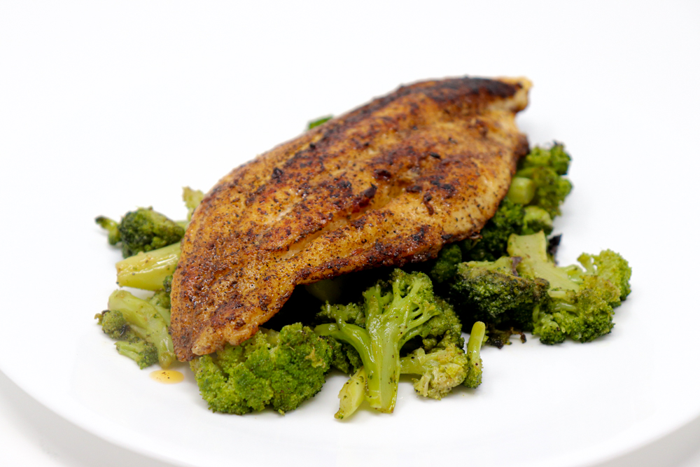 Blackened catfish fillet served over roasted broccoli on a white plate.